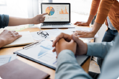 a hand pointing at a graph on a laptop screen and arms of others looking at the laptop